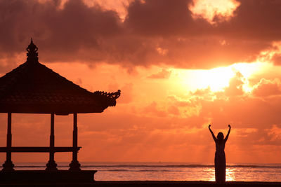 Silhouette woman on shore against sky during sunset