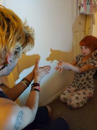 High angle view of girl sitting on floor playing shadow puppets with step father 
