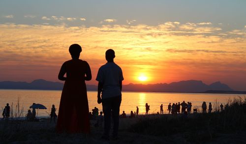 Silhouette people standing at beach during sunset