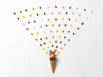 Directly above shot of multi colored candies and ice cream cone over white background