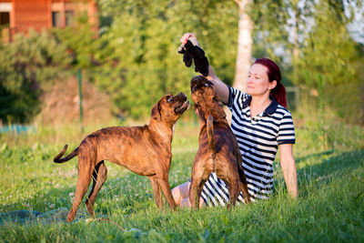 Mid adult woman playing with dogs while sitting on grassy field against sky at park