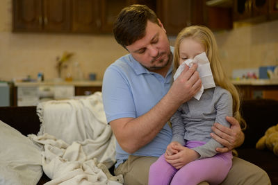 Dad wipes his sick childs nose with a white disposable paper napkin at home. the father suspects