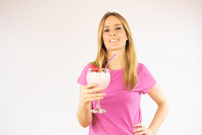 Beautiful young woman drinking glass against white background