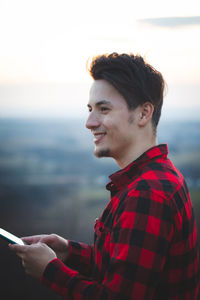 Portrait of a twenty-three year old man in a black and red checked shirt, smiling at his friend with 