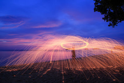 Illuminated spinning wire wool at lakeshore during night