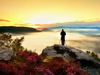 Professional photographer takes photos with mirror camera and tripod on peak of rock. dreamy nature