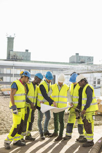 Architects and construction workers discussing over blueprint at site