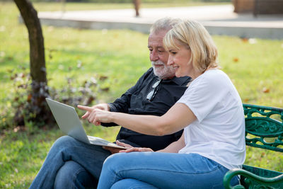 Senior man using laptop with woman on bench at park