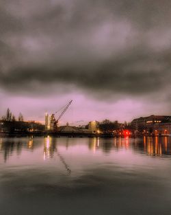 Illuminated buildings by river against sky at night