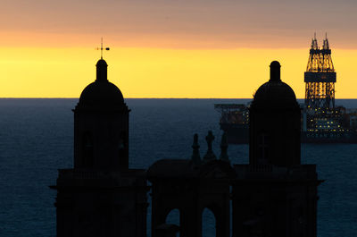 Silhouette of building by sea against sky during sunset