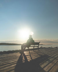 Man sitting on shore against sky during sunset
