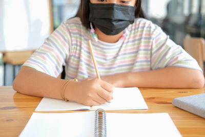 Asian girl student wearing face mask studying writing notes doing homework in library. learning 