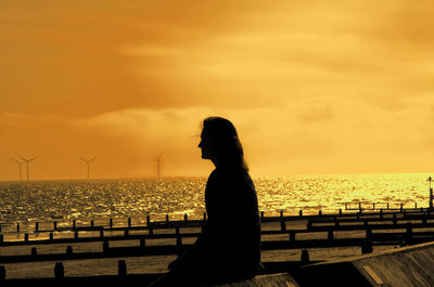 Silhouette woman standing by sea against sky during sunset