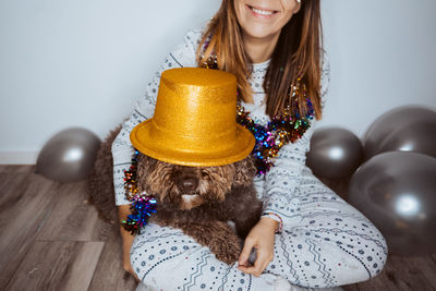 Midsection of woman carrying dog with party hat on lap at home