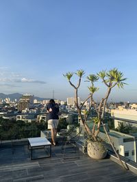 Rear view of woman standing by plants in city against sky