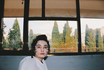 Portrait of young woman looking through window