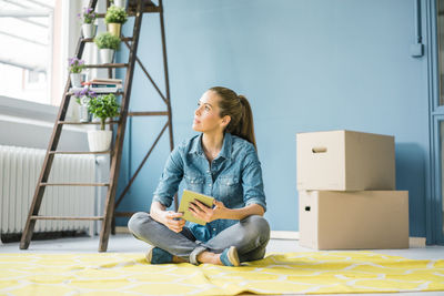 Woman sitting on floor of her new apartment, using digital tablet