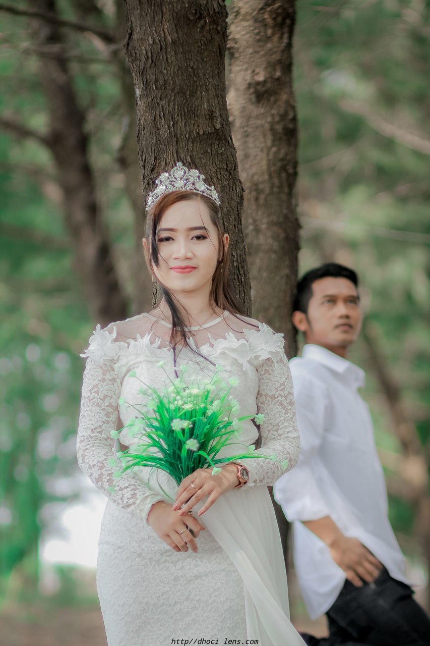 PORTRAIT OF SMILING WOMAN STANDING BY TREE