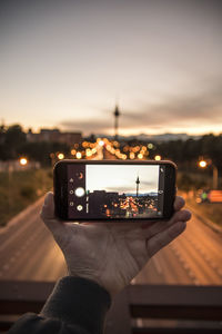 Cropped hand photographing tower in city from mobile phone at dusk