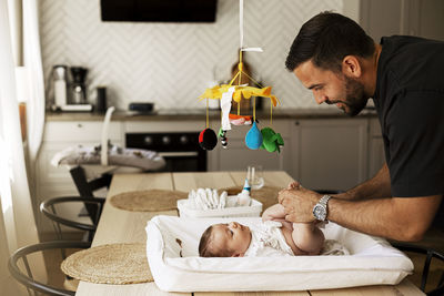 Father changing diaper of son lying down on table at home