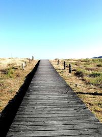 Boardwalk on field against clear sky