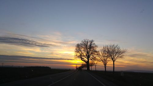 Road by silhouette trees against sky during sunset