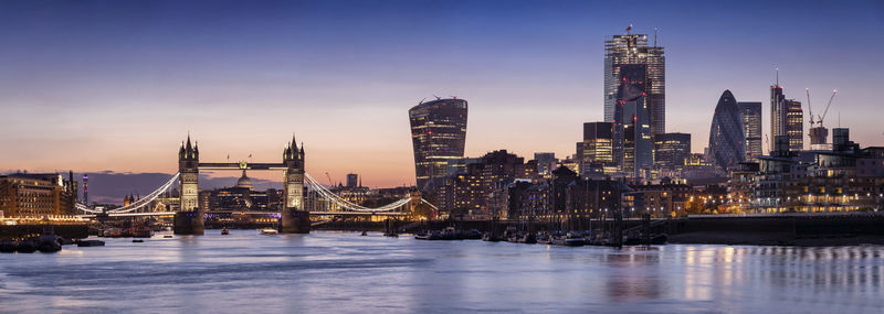 Illuminated city buildings by river against sky