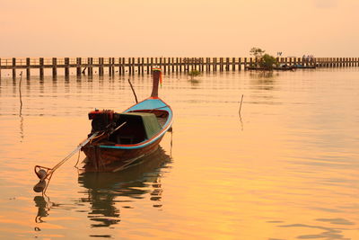 Longtail boat moored on lake against sky during sunset