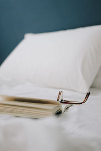 High angle view of book on bed. white sheets, glasses on it. pillows are behind.