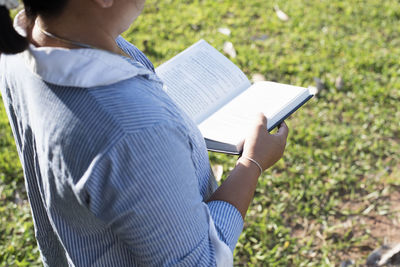 Rear view of woman reading book while standing on field