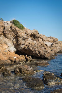 Rock formations by sea against clear blue sky