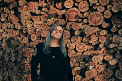 Portrait of woman standing against stacked logs