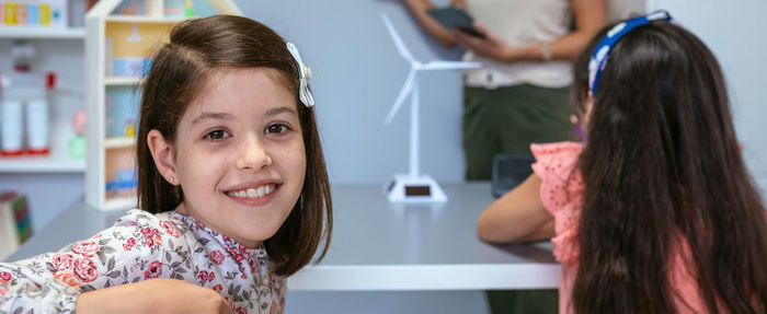 Portrait of schoolgirl in ecology classroom and teacher explaining lesson on background