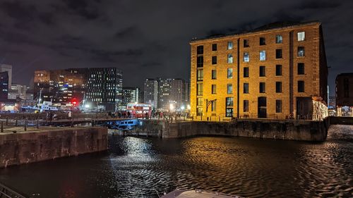 Illuminated buildings by river against sky in city at night