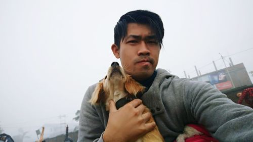 Portrait of young man holding dog against clear sky