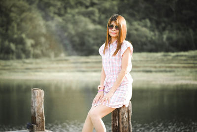 Portrait of woman in sunglasses sitting against lake