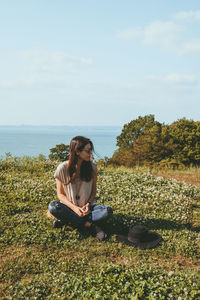 People sitting on land by sea against sky
