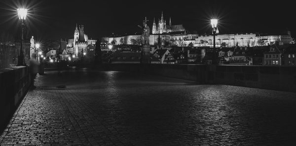 Illuminated street by buildings at night