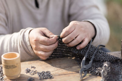 Midsection of man working on chain mail armor at table