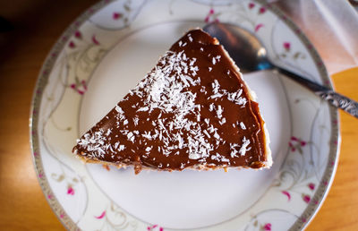 A piece of a creamy chocolate cake with coconut flakes on top on a white plate