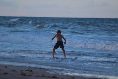 Full length of shirtless boy on beach against sky