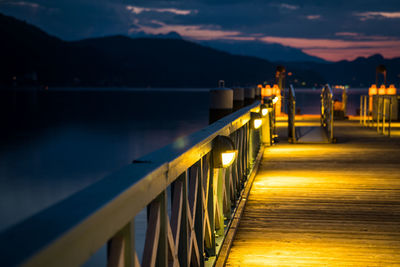 Illuminated bridge over lake against sky at sunset