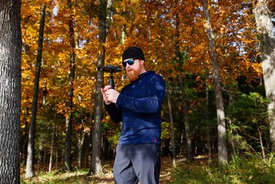 Bearded man photographing against trees during autumn