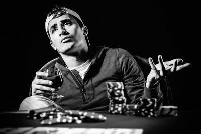 Sad man sitting at poker table with whiskey against black background