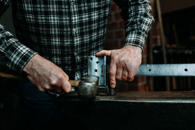 Midsection of man hammering latch in workshop