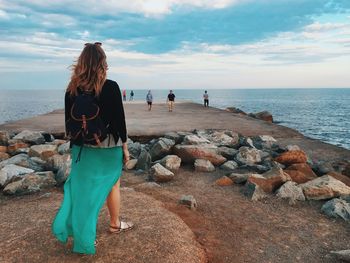 Rear view of women standing on rock at beach against sky