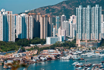 Sailboats in city by sea against modern buildings