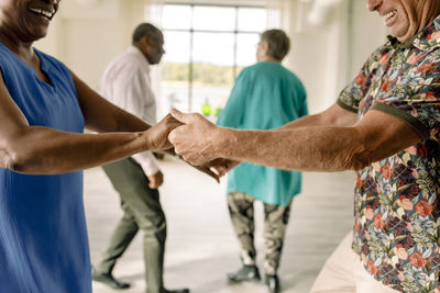 Midsection of happy senior couple holding hands while practicing dance in class