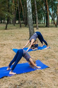 Family fitness and yoga. happy mom exercising with baby girls on grassy land against trees in