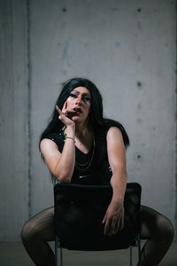 Young woman sitting on chair against wall